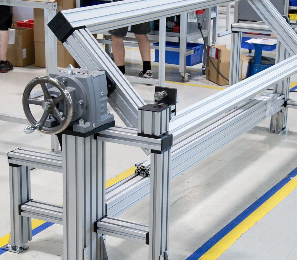 Modularer, schwenkbarer Arbeitstisch von Robotunits mit stabiler Aluminiumprofilkonstruktion und integrierter Handkurbel. Die Neigungsverstellung ermöglicht eine ergonomische Anpassung der Arbeitsfläche an verschiedene Arbeitsschritte. Ideal für flexible Montage- und Prüfprozesse in der Fertigung.