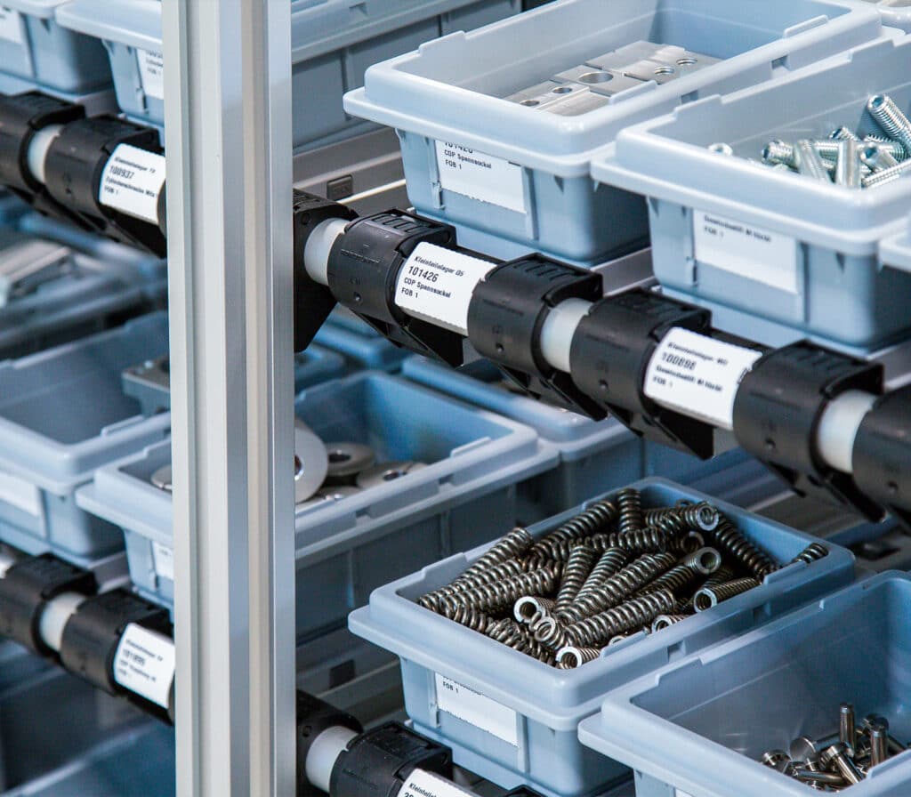 Detailansicht eines Robotunits Rüstwagens, aufgebaut aus dem Automatisierungsbaukasten, mit integrierten Rollenbahnen zur ergonomischen Materialbereitstellung (MBS). Bestückt mit beschrifteten Kleinladungsträgern (KLTs) für Schrauben, Federn und Metallteile – ideal für strukturierte, effiziente Montagevorbereitung und Nachschubversorgung.